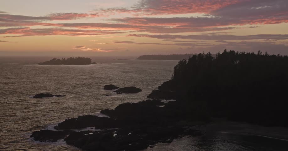 A beautiful aerial view of a rugged, rocky Pacific coastline silhouetted against a colorful sunset sky
