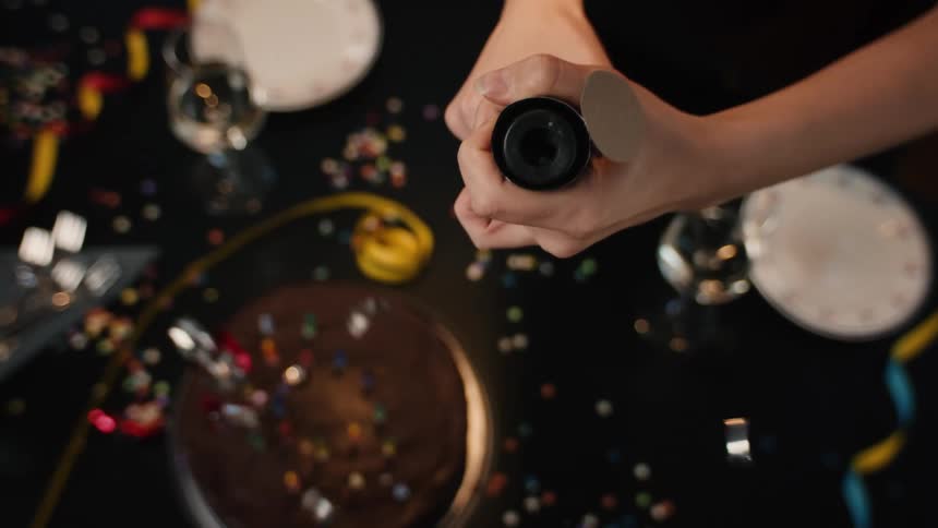 A top-down slow-motion view of a person setting off a party popper, showering a birthday cake and table with confetti