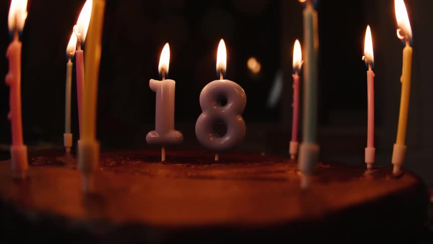 Candles spelling out the number 18 flicker brightly on a chocolate birthday cake in a dark room
