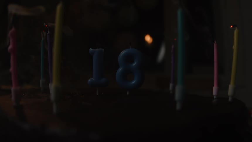 Slow motion close-up of colorful candles spelling out the number 18 being blown out on a birthday cake in a dark room