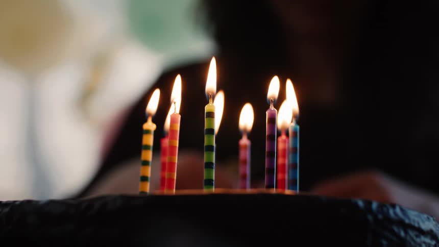A close-up shot of colorful birthday candles flickering on a cake against a dark background
