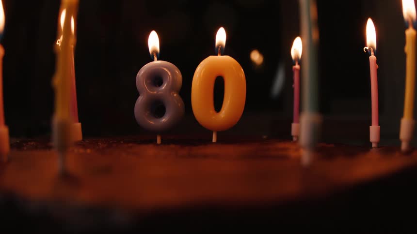 A hand with a lighter illuminates the number 80 candles on a cake for an eightieth birthday celebration