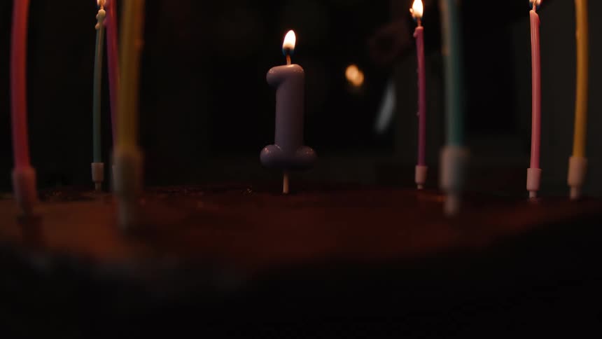 A hand uses a lighter to light a number one candle on a chocolate first birthday cake in a dark room