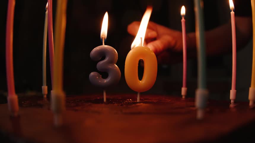 A hand uses a match to light the number 30 candles on a birthday cake in slow motion