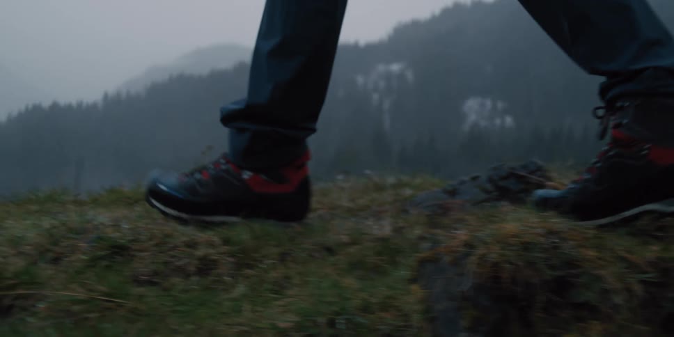 A close-up slow-motion shot of hiking boots walking along a grassy mountain path on a foggy day