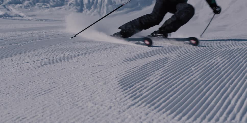 Slow motion shot of a skilled skier carving clean turns on a fresh corduroy ski slope