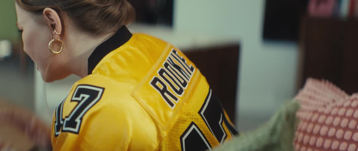 Close-up over the shoulder shot of a young woman wearing a yellow 'ROOKIE' football jersey while laughing