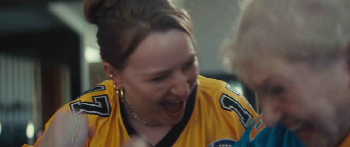 A young woman and her elderly mother cheer and fist bump while watching an American football game on a tablet at home