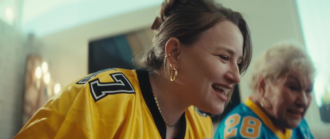 Excited adult daughter and elderly mother in football jerseys celebrate wildly while watching a game together on a tablet