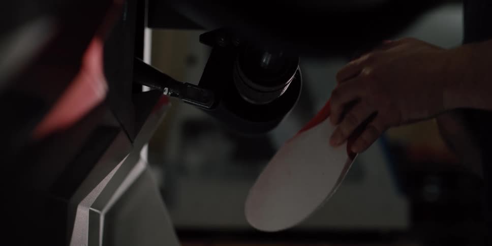 A craftsman meticulously shapes the edge of a shoe insole using a sanding machine in a workshop