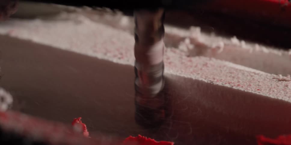 Extreme close-up slow-motion shot of a CNC machine's router bit precisely milling through a red and white foam block