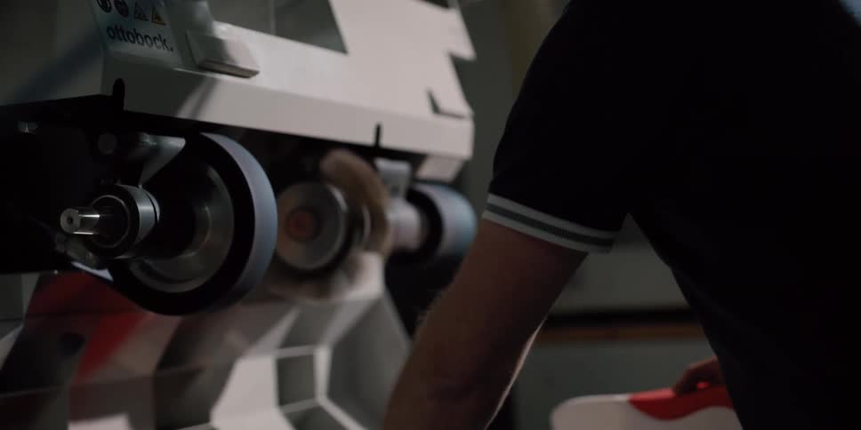 A skilled craftsman meticulously shapes and polishes a custom orthopedic product on an industrial sanding machine in a dimly lit workshop