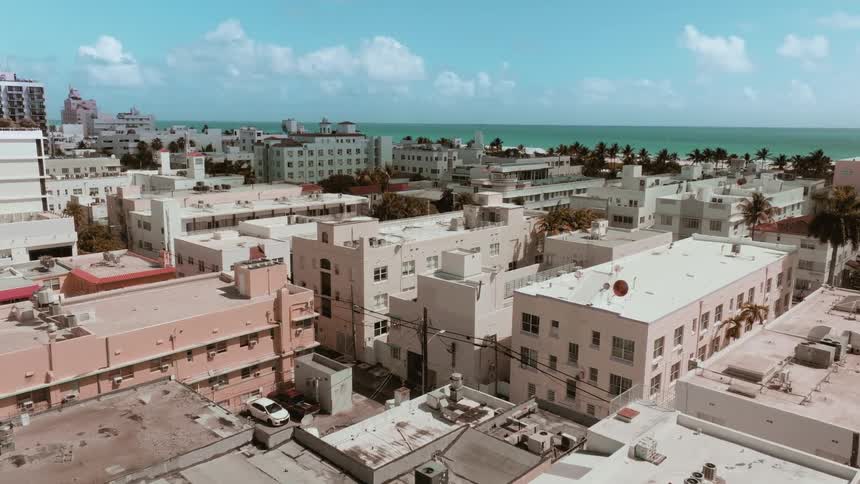 A slow aerial dolly shot pushes in over the art deco buildings and rooftops of Miami's South Beach towards the beautiful ocean