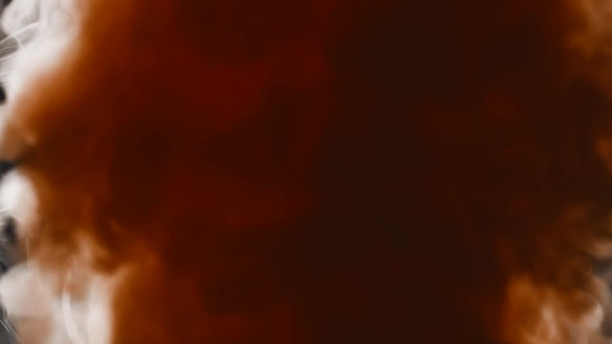 Turbulent clouds of fiery orange smoke and ethereal white vapor billow in slow motion against a black background