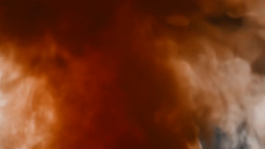 Ethereal clouds of reddish-brown and white vapor mix and flow in slow motion against a dark background