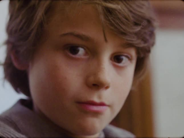 Vintage film-style extreme close-up of a thoughtful young boy turning to look directly at the camera