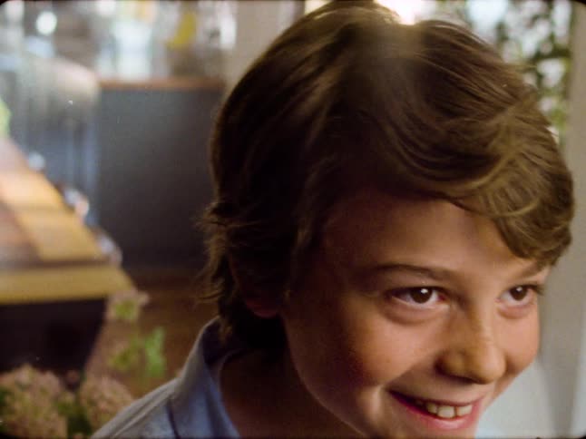 Portrait of a smiling young boy captured in a nostalgic, 8mm home movie aesthetic