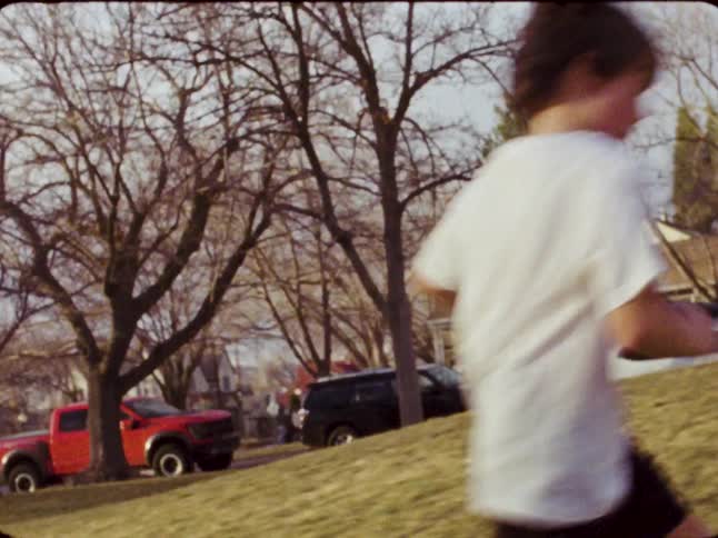 Vintage 8mm footage of a young boy dribbling a soccer ball and running in a sun-drenched park