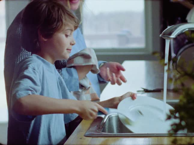 A young boy and his mom share a sweet moment doing the dishes together in the kitchen