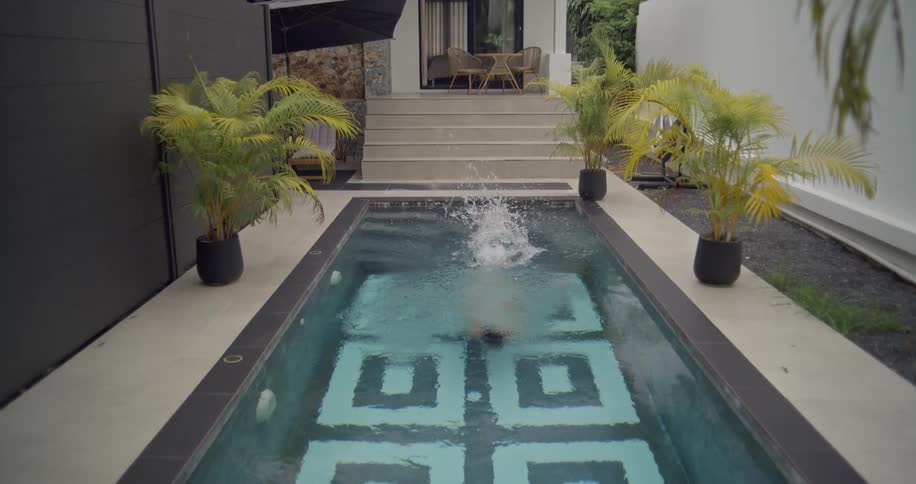 A beautiful woman in a white swimsuit gracefully dives into a private swimming pool at a modern villa in slow motion