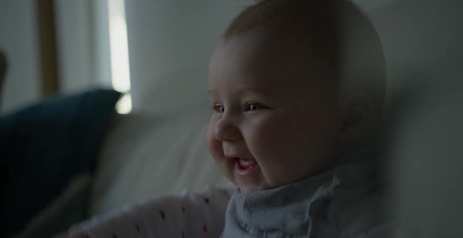 A baby smiles and laughs while raising one arm in front of himself