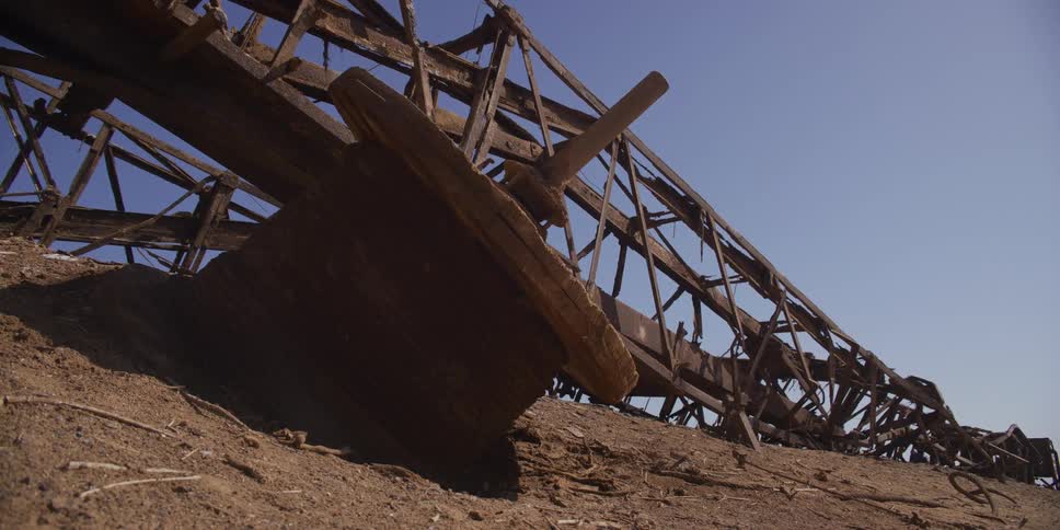 A close up of an old abandoned and rusted metal oil derrick structure on a sandy beach
