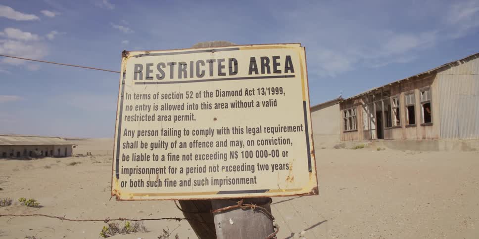 A weathered "Restricted Area" sign on a barbed wire fence warns trespassers at an abandoned diamond mining ghost town in the desert