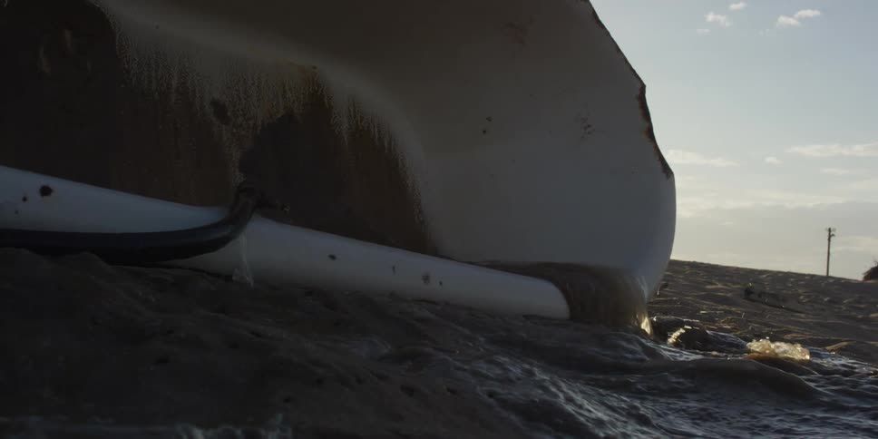A bathtub sitting on the sand overflows with water in a dramatic slow-motion close-up shot