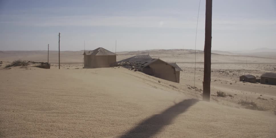 Wind blows sand over the dilapidated and abandoned buildings of a desert ghost town