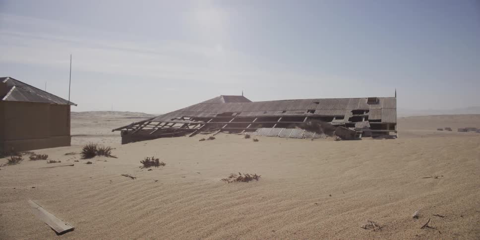 A powerful sandstorm rages across the desert, burying an abandoned, dilapidated building under blowing sand