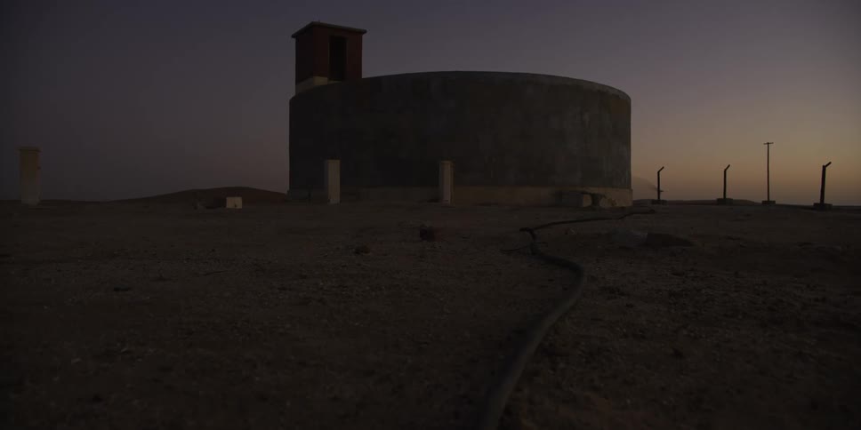 A solitary concrete water tank stands in a desolate desert landscape during twilight in a slow dolly shot