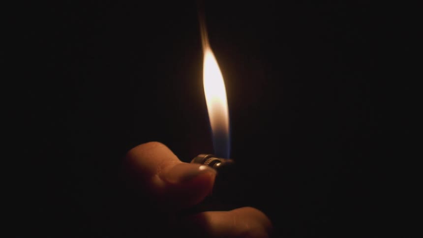 Hand ignites a lighter in the dark