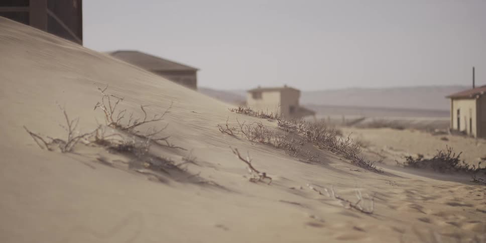 Drifting sand blows over a dune in an abandoned desert town on a hazy day