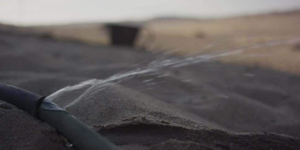 Close up shot of a leaking water pipe spraying precious water onto the dry sand in the desert
