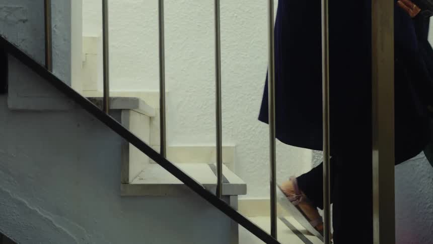 A person wearing sandals and dark pants slowly walks up a bright, white staircase with a metal railing