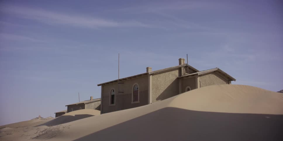 Abandoned buildings are slowly being swallowed by large sand dunes in a desert ghost town