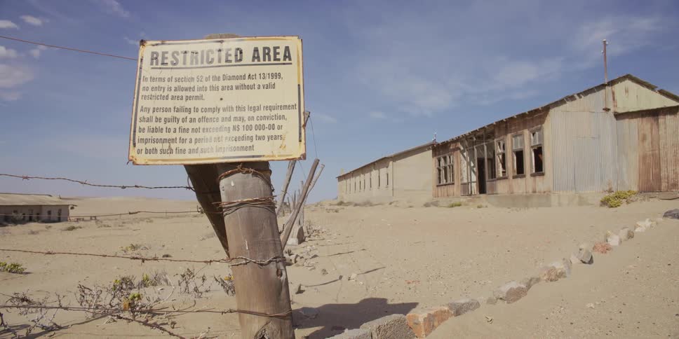 A weathered 'Restricted Area' sign on a barbed wire fence warns visitors away from an abandoned ghost town in the desert