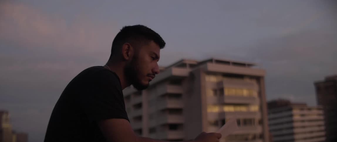A man stands on a rooftop overlooking a city at sunset