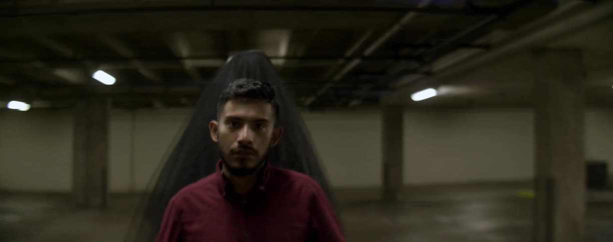 A paranormal figure wraps around a man in a parking garage