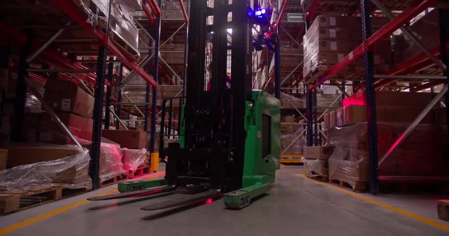 A modern forklift with flashing safety lights drives through an aisle in a vast industrial warehouse
