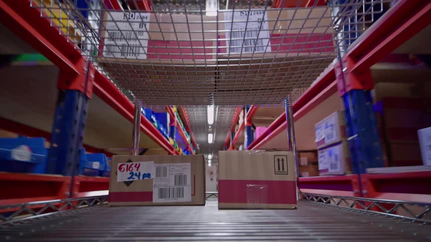 A point-of-view shot from a cart moving down a long aisle in a large, busy warehouse