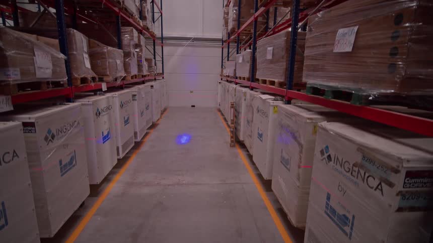 A smooth cinematic reveal shot moving through a large warehouse aisle, slowly rising to show tall shelves packed with inventory