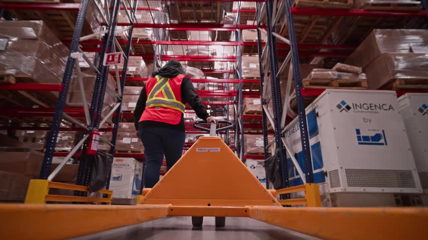 Point-of-view shot from a pallet jack as a worker navigates a long aisle in a large industrial warehouse