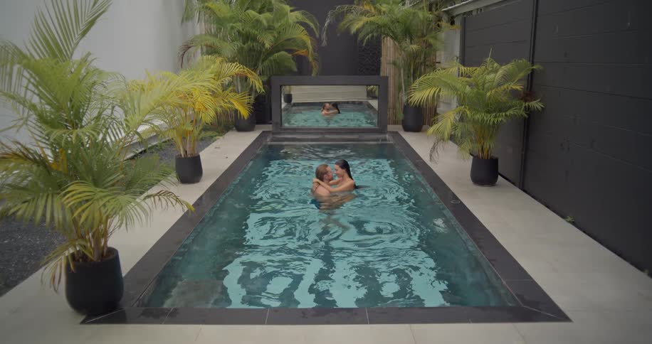 A romantic couple swims towards each other and shares an intimate kiss in a luxurious, modern private pool