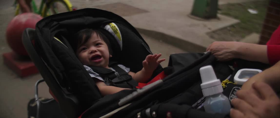 A baby in a stroller is smiling and reaching its hand up