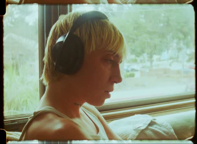 Young person wearing headphones sits thoughtfully by a sunlit window in a vintage home interior