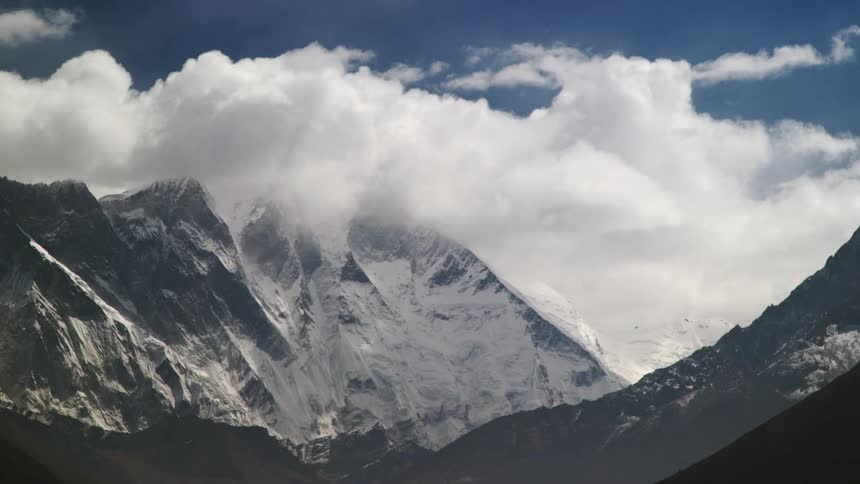 Puffy, white clouds flow over a tall mountain range
