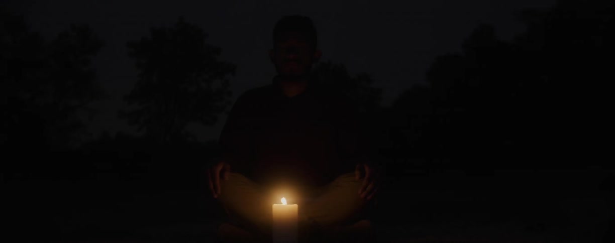 A single candle is near a sitting man at night