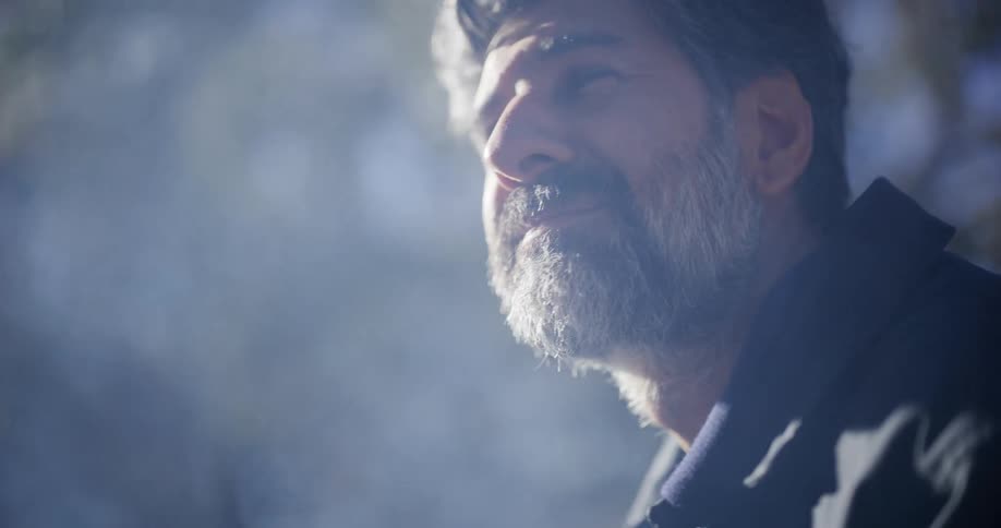 Close up of a middle-aged man with a salt and pepper beard smiling gently as he looks up through a hazy atmosphere