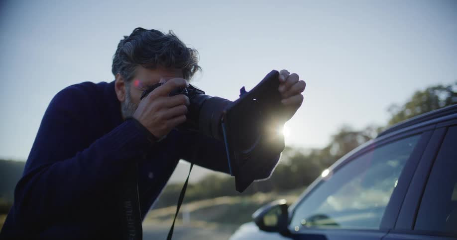 A professional automotive photographer uses a Fujifilm camera with a matte box to shoot a car against the bright sun